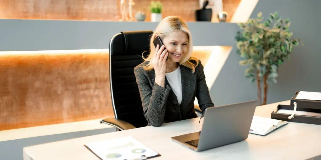 Geschäftsfrau telefoniert am Schreibtisch, arbeitet am Laptop, modernes Büro.
