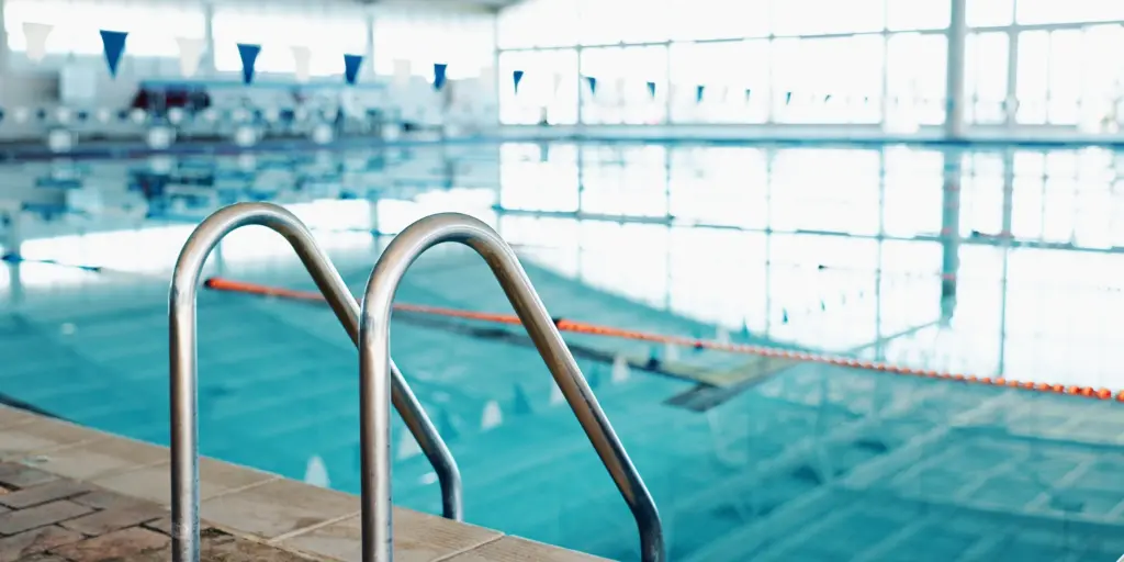 Modernes Hallenbad mit Edelstahlleiter und heller Fensterfront. Ideal für Sport und Entspannung.