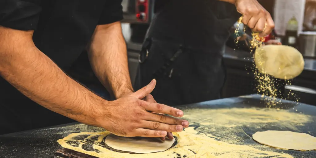 Bäcker formt Teig auf bemehlter Arbeitsfläche, Vorbereitung von Brot oder Pizza, handgemachte Backkunst.