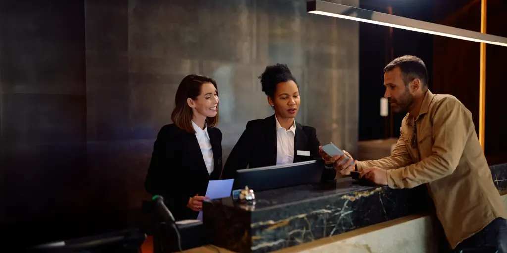 Ein Mann checkt an einem eleganten Hotelrezeption ein, spricht mit zwei Mitarbeiterinnen in Uniform.