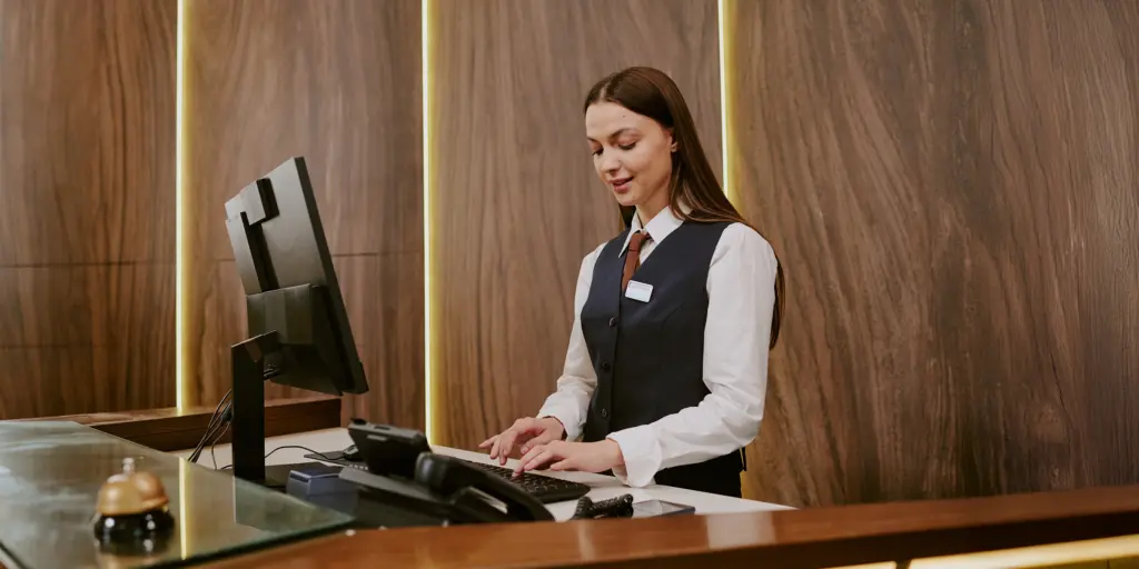 Rezeptionistin am Schalter, arbeitet an einem Computer, elegante Holzverkleidung, Hotelambiente, professionelle Atmosphäre.