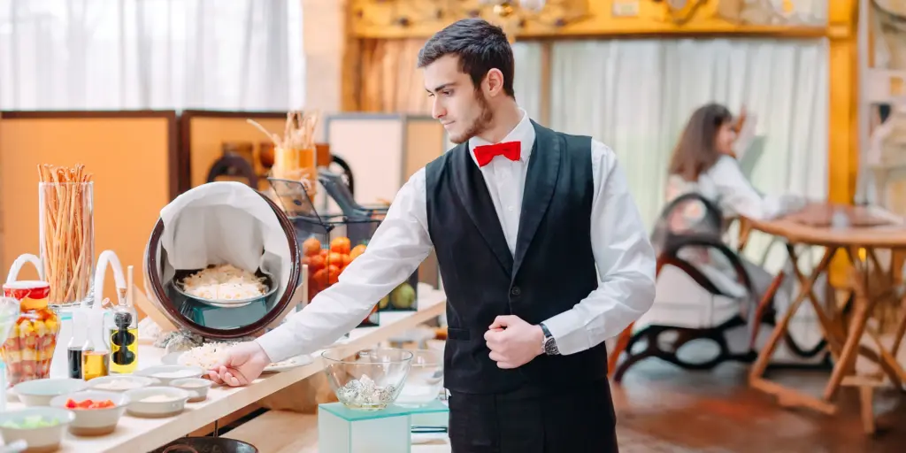 Kellner mit roter Fliege serviert am Buffet in elegantem Restaurant, Gast im Hintergrund.